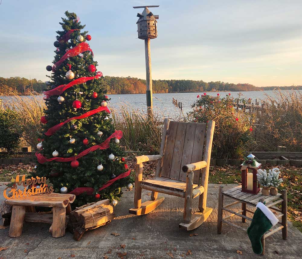 A Christmas tree and wooden chair with side table with Lake Marion in the background. Ready for Santa to visit and take pictures with lucky children.